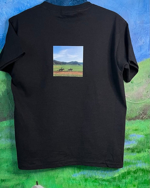 Black t-shirt with a small square print of a landscape on a grassy background